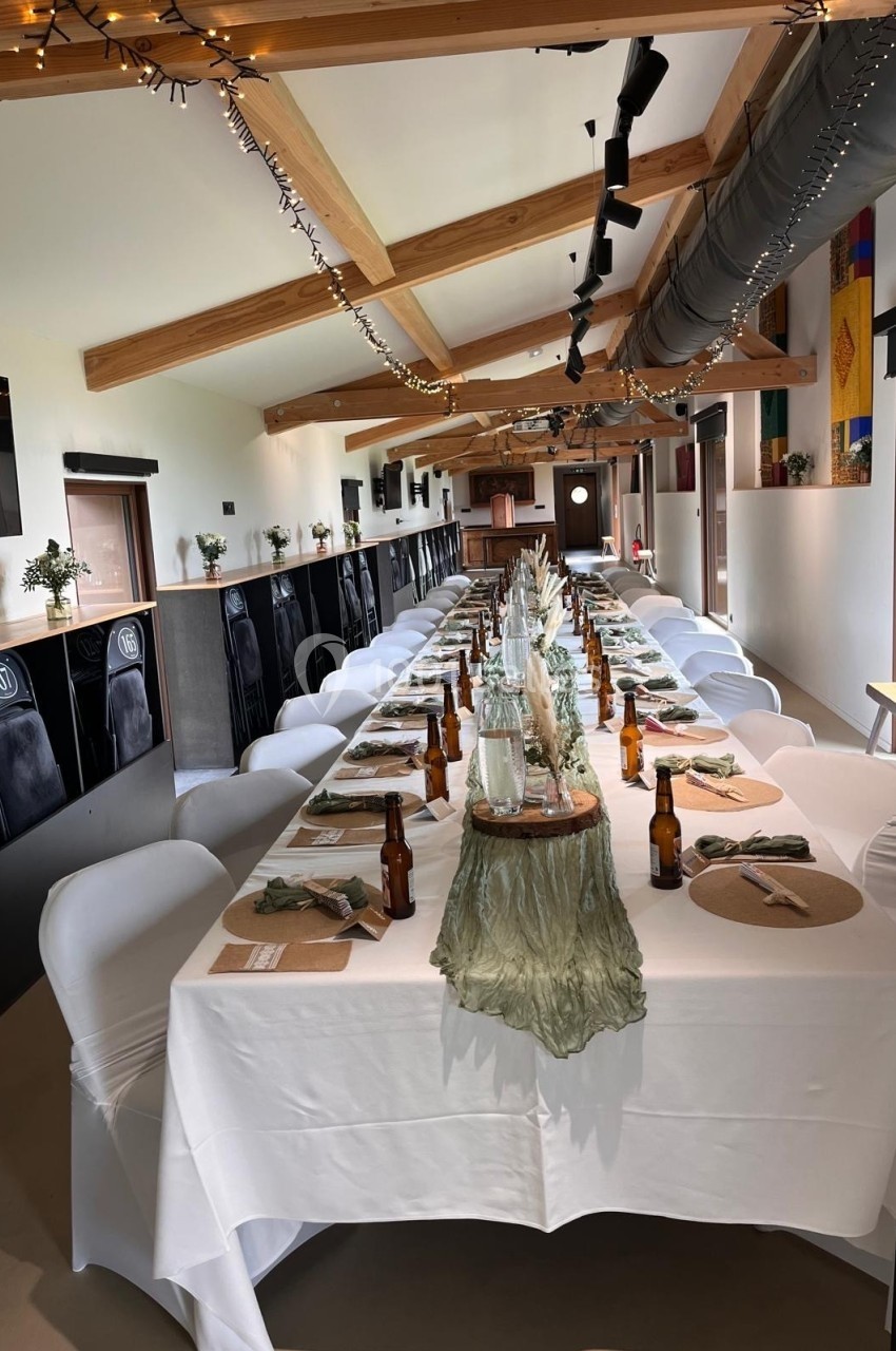 Grande table dressée pour un repas, décorée avec des fleurs séchées, nappes blanches et chaises couvertes, dans une salle…