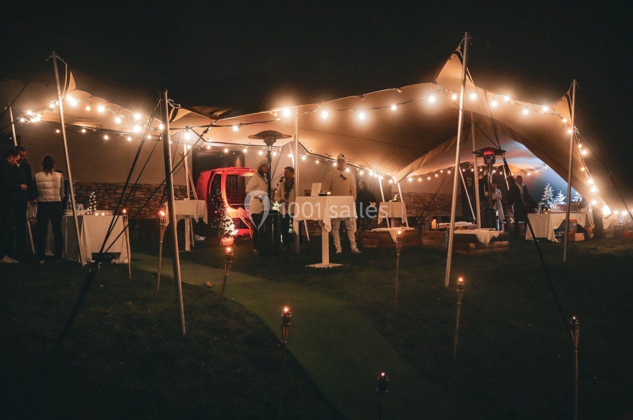 Tente éclairée par des guirlandes lumineuses lors d'un événement nocturne avec invités et tables dressées.