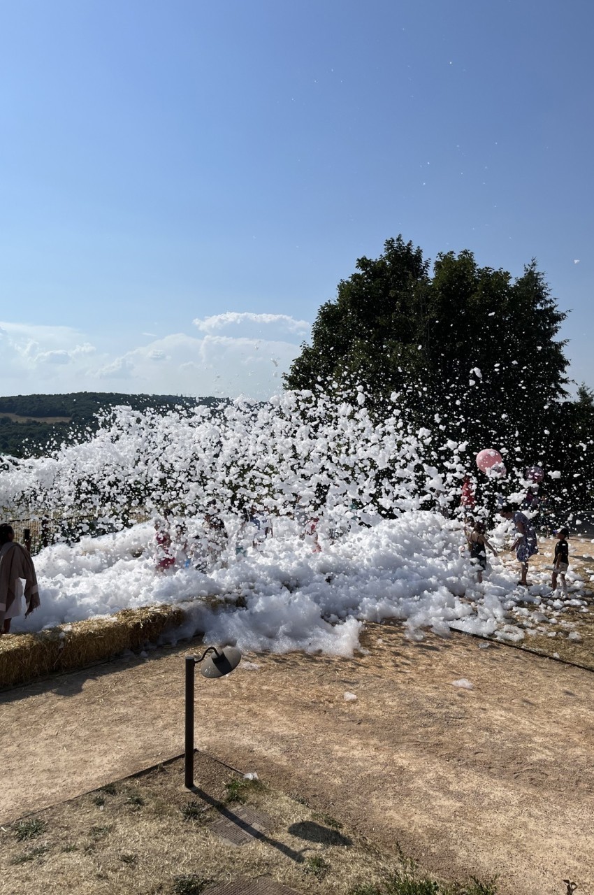 Des enfants jouent dans une grande quantité de mousse en plein air, sous un ciel dégagé.