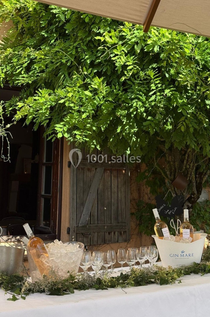 Table dressée en extérieur avec verres, seaux à glace et bouteilles de vin, devant un mur végétalisé.