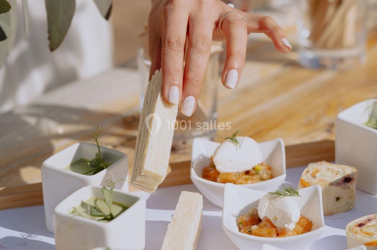 Une main prend un sandwich au milieu d'une table garnie de verrines et d'amuse-bouches variés.