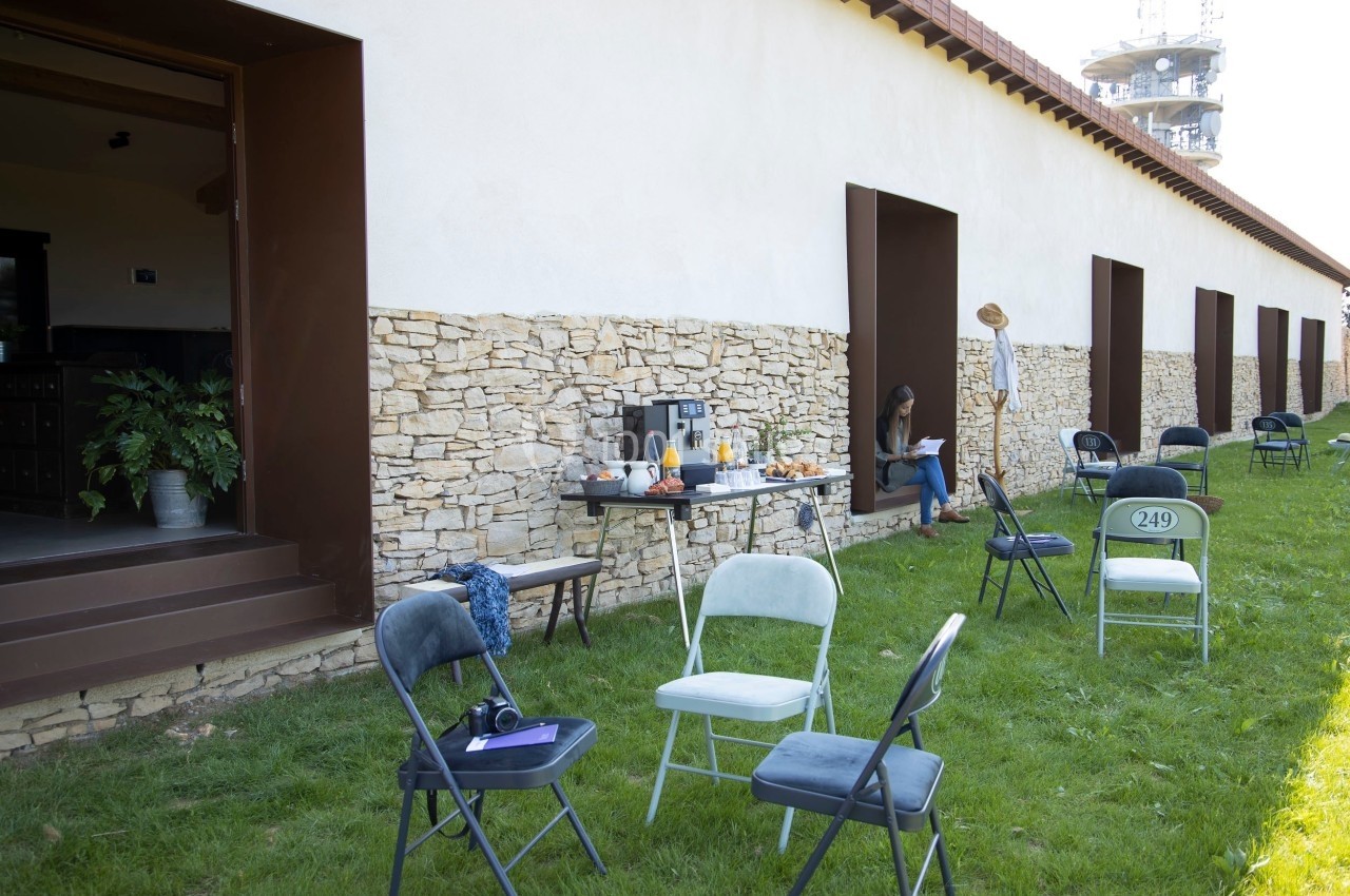 Chaises dispersées sur une pelouse devant un bâtiment en pierre, avec une table contenant des boissons et des collations.