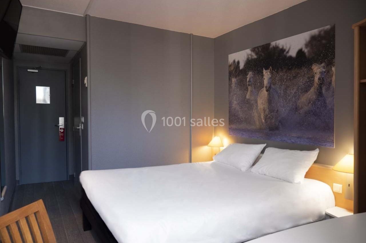 Chambre d'hôtel moderne avec lit double, mur gris, éclairage doux et tableau représentant des chevaux dans l'eau.