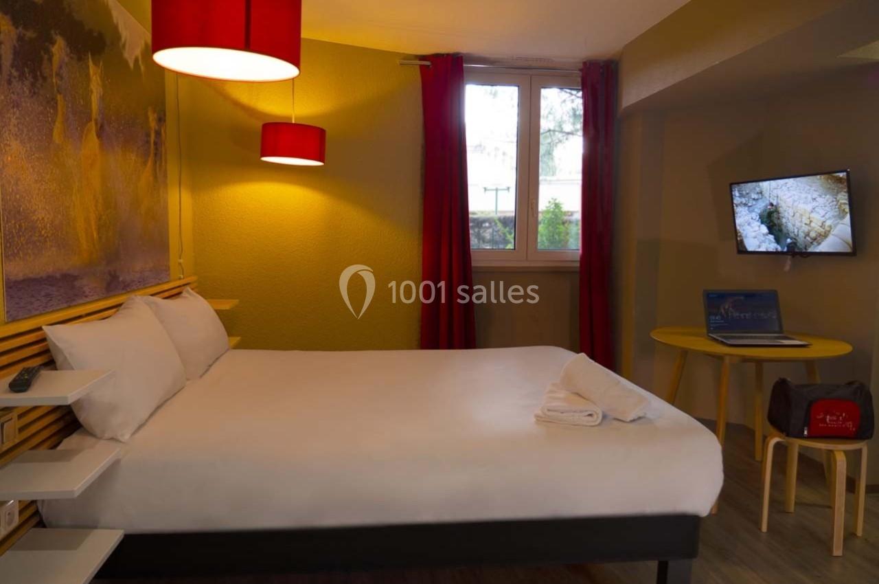 Chambre d'hôtel avec lit double, murs jaunes, rideaux rouges, télévision allumée et bureau avec ordinateur portable.