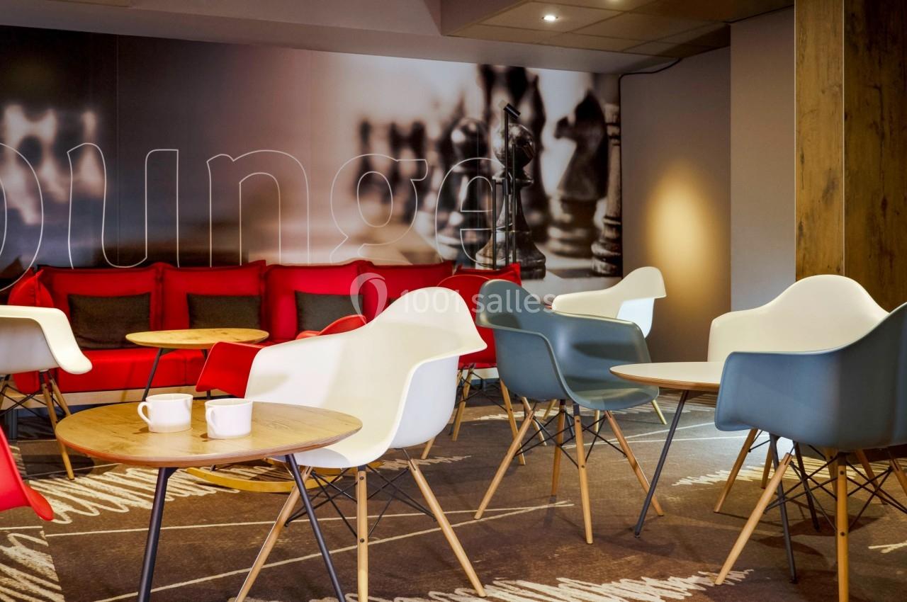 Espace lounge avec fauteuils modernes, tables basses en bois et mur décoré d'une image d'échiquier.