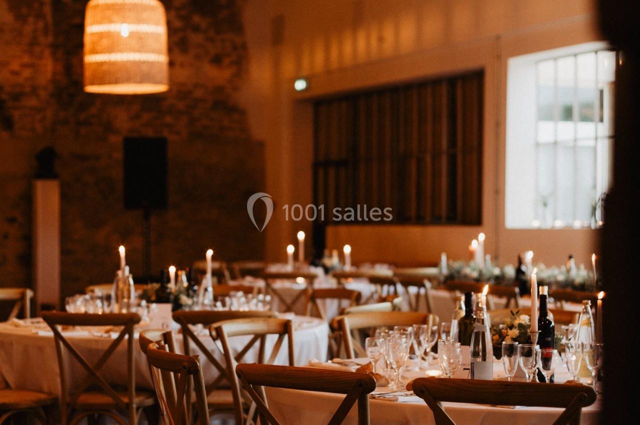 Salle de réception chaleureuse avec tables dressées, éclairage tamisé et guirlandes lumineuses suspendues.