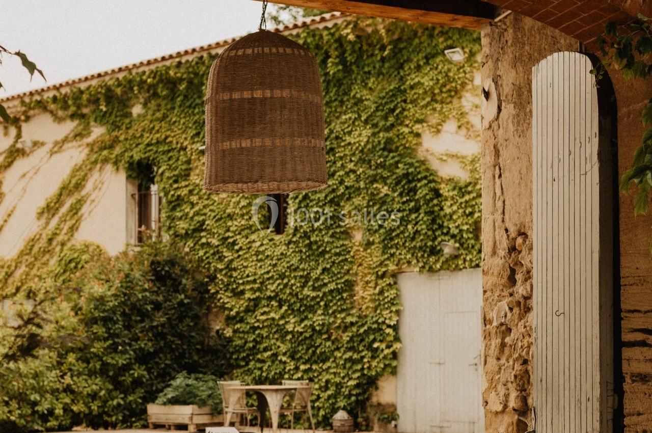 Cour intérieure avec murs recouverts de lierre, une porte en bois ouverte, un tonneau et une lanterne suspendue.