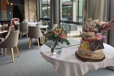 Chambre avec lit double, mur décoré de papier peint tropical, poutre apparente et grande fenêtre avec rideaux beiges.