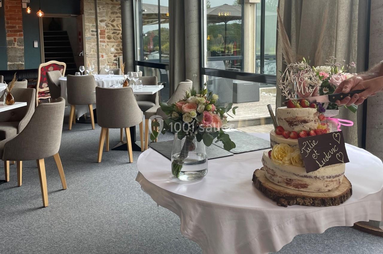 Gâteau de mariage décoré de fruits et fleurs sur une table ronde, dans une salle de réception lumineuse.