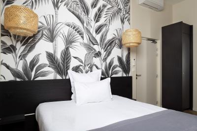 Chambre avec lit double, mur décoré de papier peint tropical, poutre apparente et grande fenêtre avec rideaux beiges.