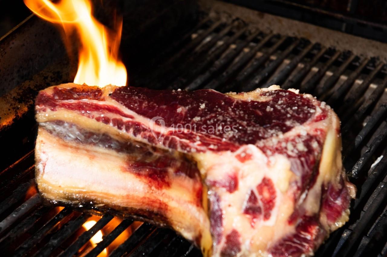 Bifteck épais en train de griller sur un barbecue avec une flamme visible.