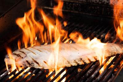 Assiette contenant un poisson entier grillé, des légumes rôtis variés et une sauce servie sur une table en marbre.
