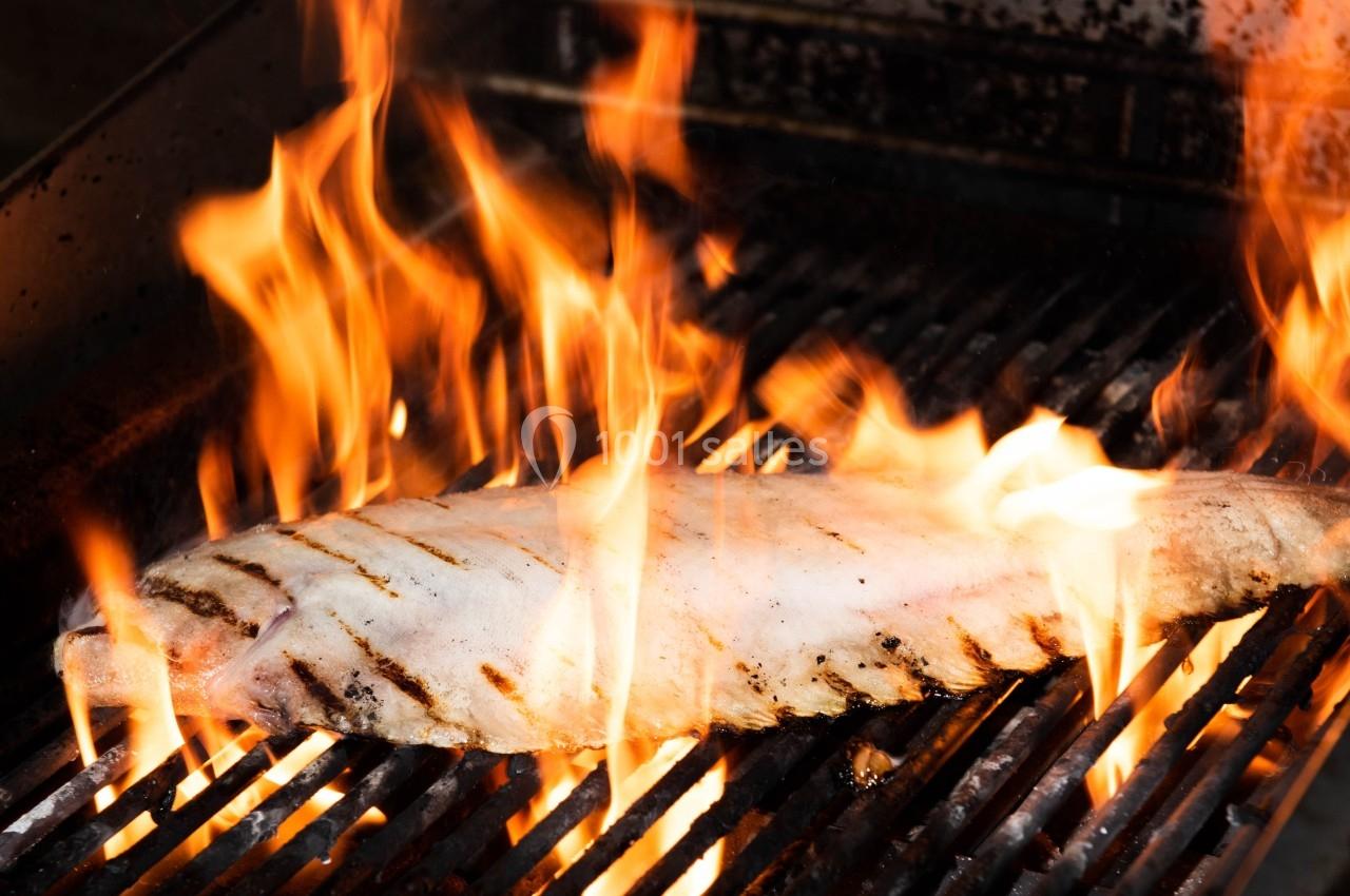 Poisson entier grillé sur un barbecue, entouré de flammes vives.