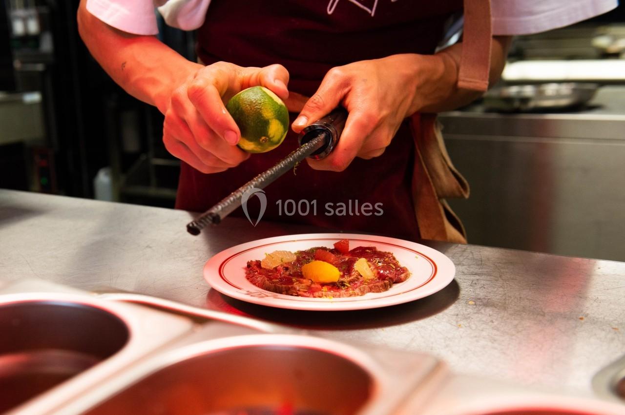 Un cuisinier râpe un citron vert au-dessus d'une assiette garnie de fruits et de préparation culinaire.