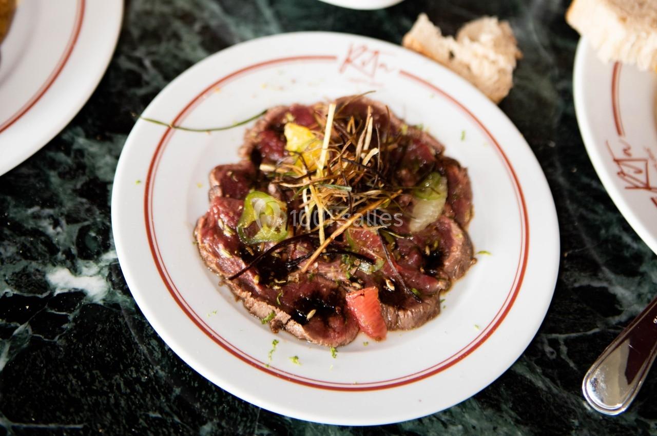 Assiette de carpaccio de bœuf garnie de légumes, herbes et filet de sauce, servie sur une table en marbre.