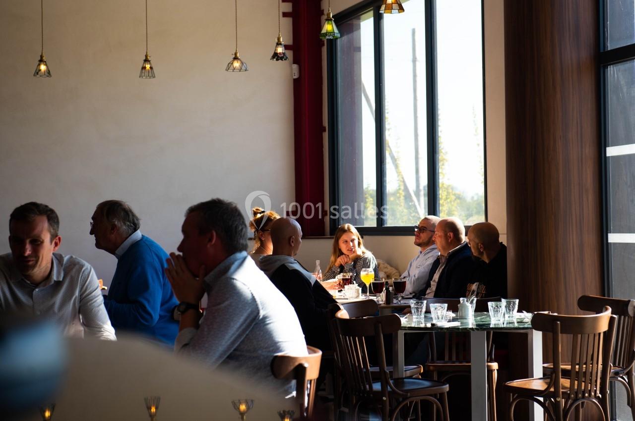 Des personnes assises à des tables dans un restaurant lumineux, discutant et partageant un repas près de grandes fenêtres.