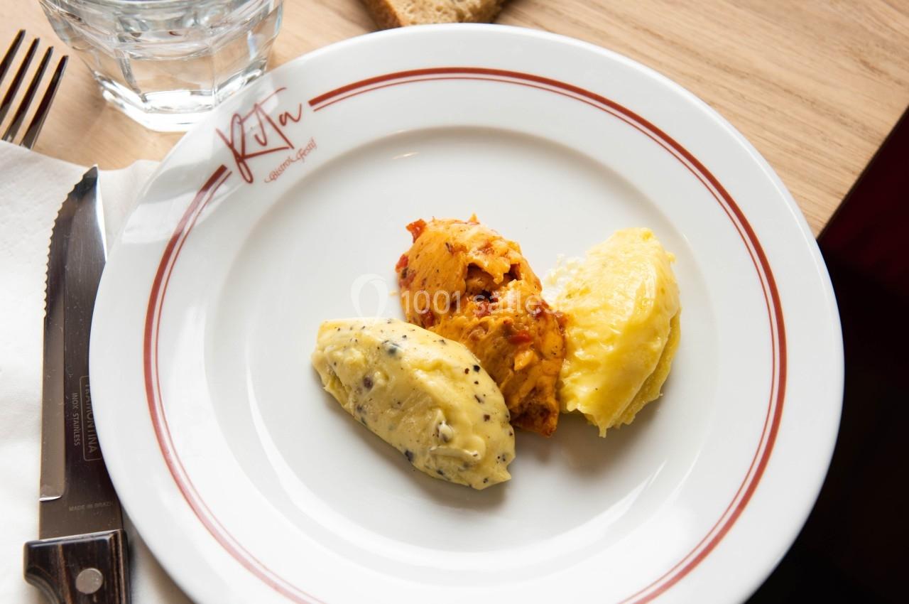 Assiette contenant trois quenelles de beurre aromatisé, posée sur une table en bois avec couteau, pain et verre d'eau.
