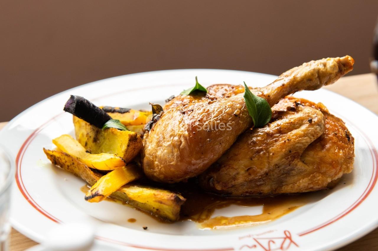 Assiette de poulet rôti accompagné de légumes grillés, servie sur une table en bois avec une théière blanche à côté.
