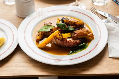 Des personnes assises à des tables dans un restaurant lumineux, discutant et partageant un repas près de grandes fenêtres.