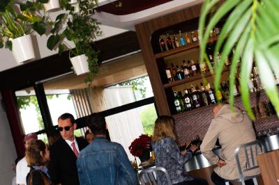 Des personnes assises à des tables dans un restaurant lumineux, discutant et partageant un repas près de grandes fenêtres.
