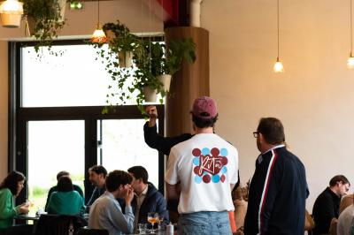 Des personnes assises à des tables dans un restaurant lumineux, discutant et partageant un repas près de grandes fenêtres.