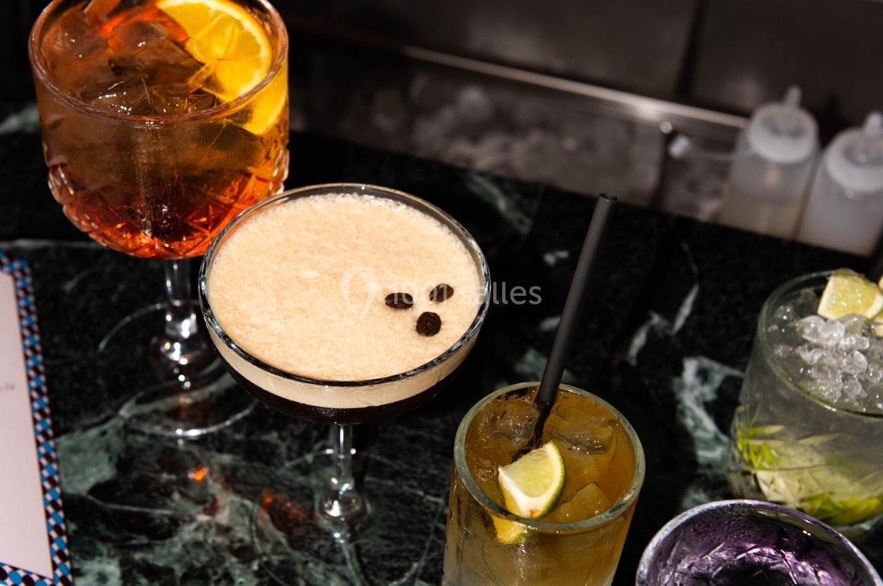 Cinq cocktails variés sur un comptoir en marbre vert, chacun avec une garniture différente.