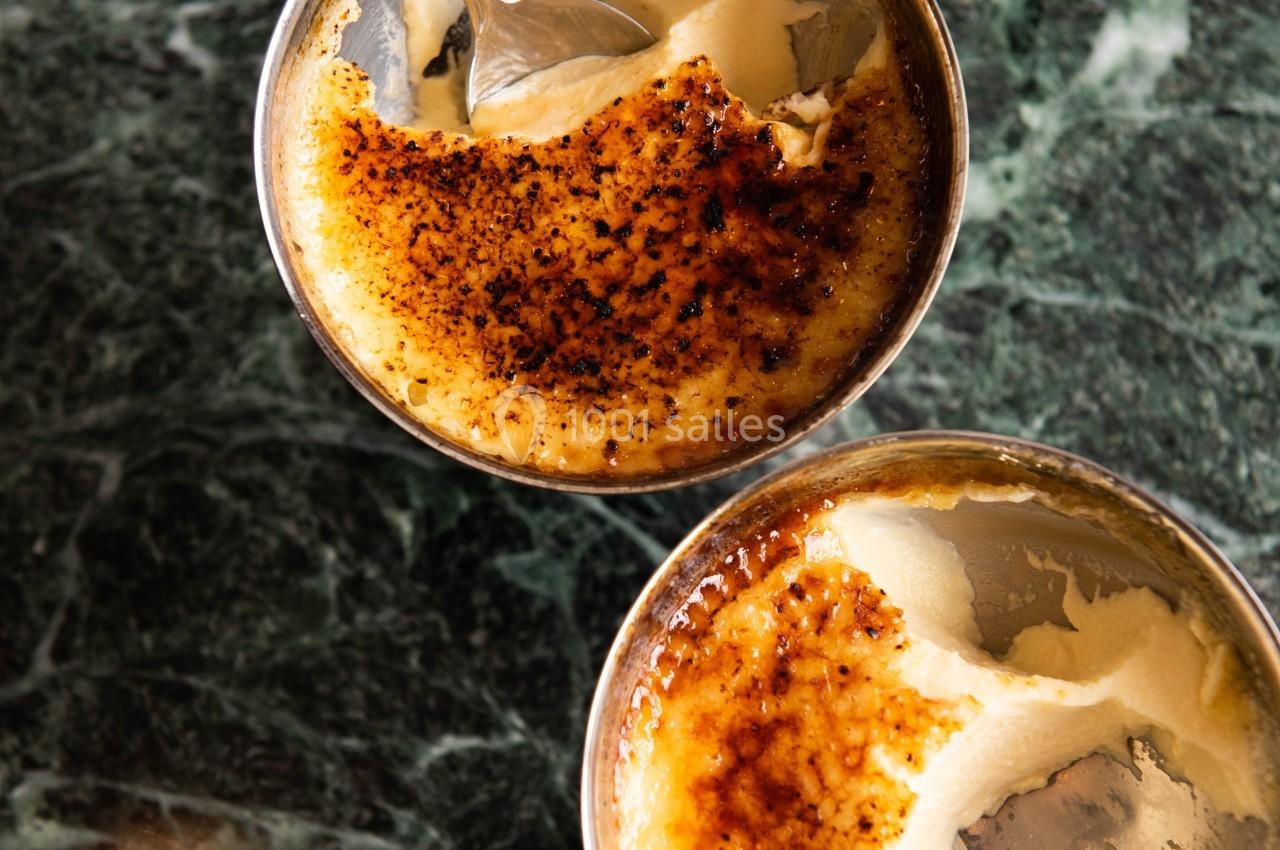Deux crèmes brûlées avec une croûte caramélisée dorée, partiellement cassée, servies dans des ramequins sur une table en…