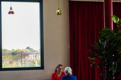 Des personnes assises à des tables dans un restaurant lumineux, discutant et partageant un repas près de grandes fenêtres.