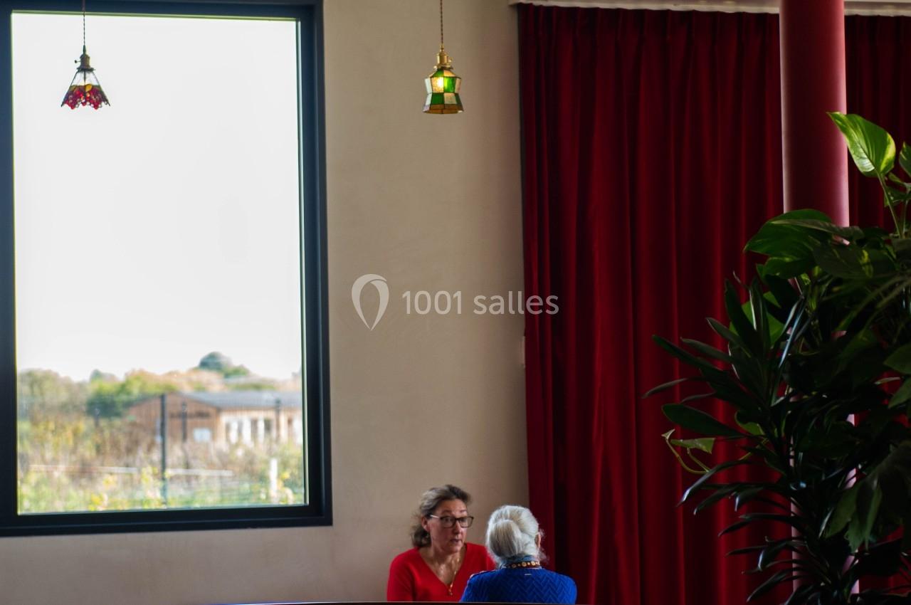 Deux personnes discutent à une table dans un restaurant lumineux avec des rideaux rouges et des lampes suspendues.