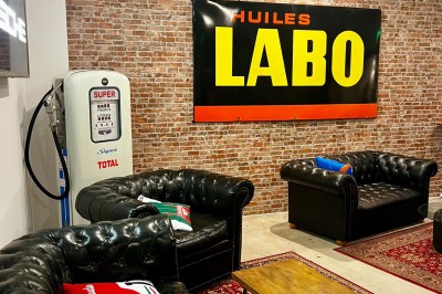 Tables hautes noires dans une salle avec un mur décoré d'une photo de voiture de course vintage.