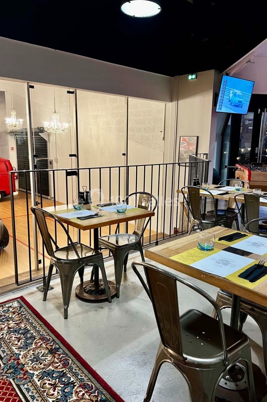 Salle de restaurant moderne avec tables en bois, chaises en métal et vue sur une exposition de voitures anciennes.