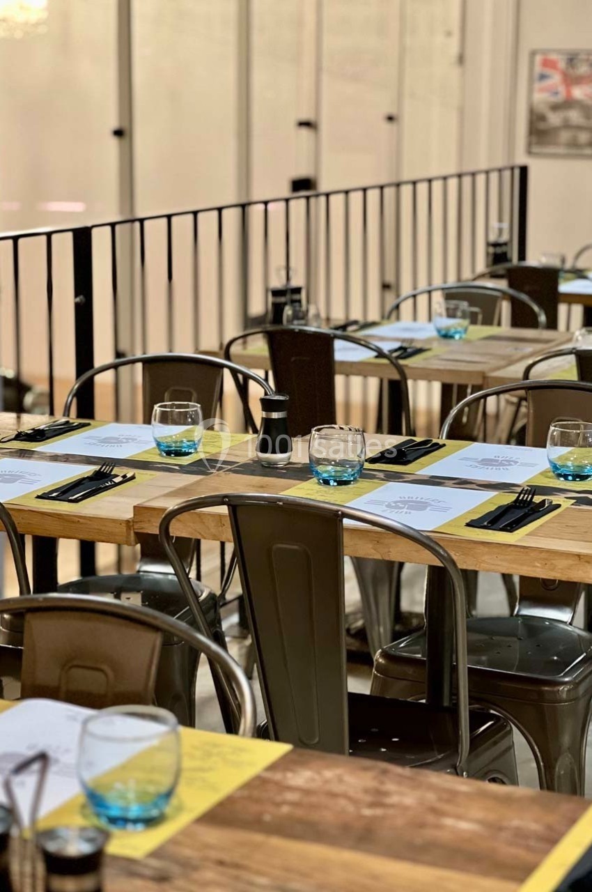 Tables en bois dressées avec couverts, verres et sets de table dans un restaurant à l'ambiance moderne et épurée.