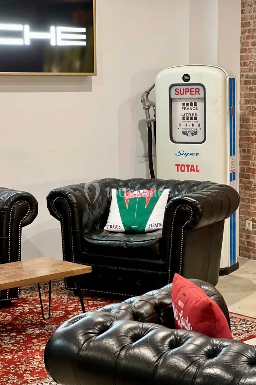 Fauteuils en cuir noir dans un salon rétro avec une ancienne pompe à essence et un mur en briques.