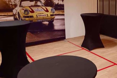 Tables hautes noires dans une salle avec un mur décoré d'une photo de voiture de course vintage.