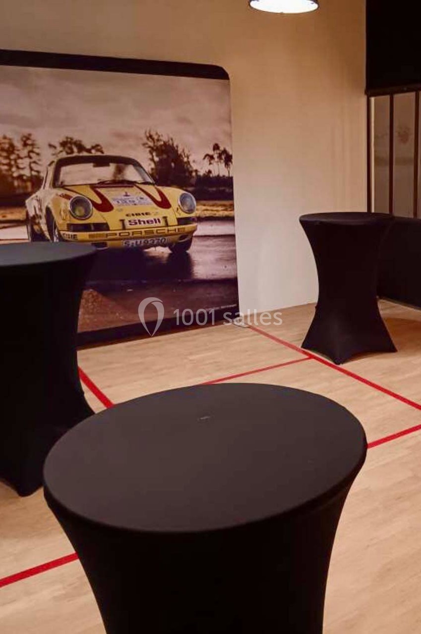 Tables hautes noires dans une salle avec un mur décoré d'une photo de voiture de course vintage.