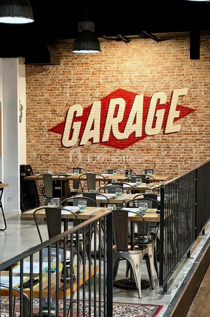 Salle de restaurant au style industriel avec mur en briques et inscription ’Garage’ en lettres rouges.