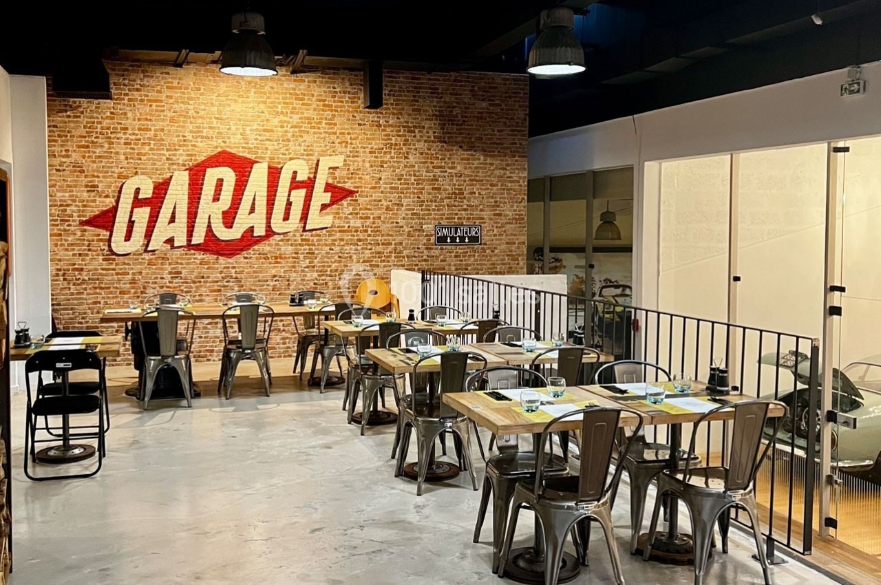 Salle de restaurant au style industriel avec murs en briques, mobilier métallique et enseigne ’Garage’ sur le mur.