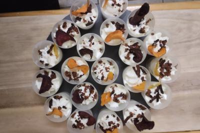 Plateau en bois avec verrines garnies, bol de pain tranché et bouteille de vin mousseux en arrière-plan.