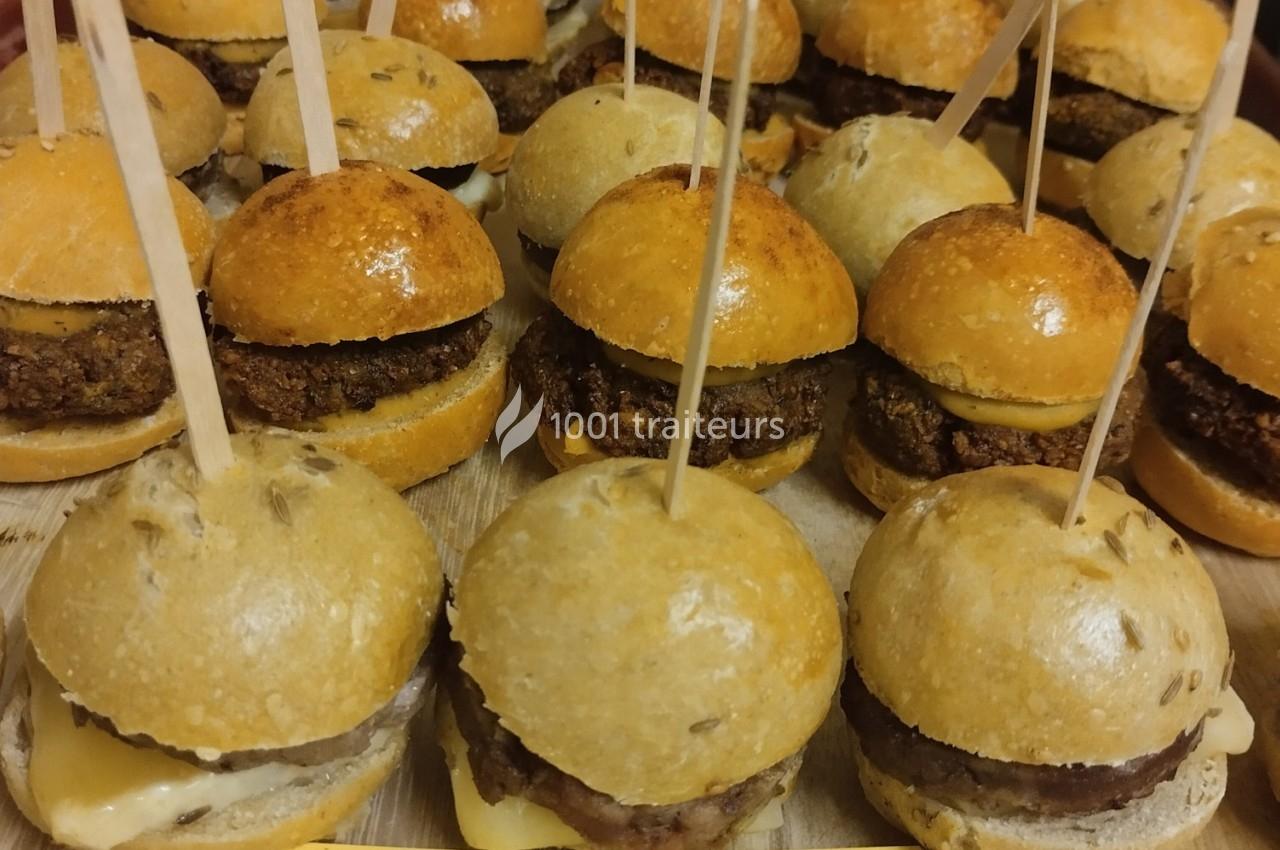 Mini-burgers alignés sur une surface en bois, garnis de fromage et de galettes, maintenus par des piques en bois.