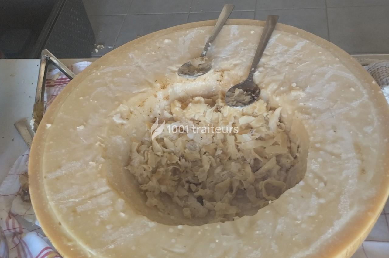 Meule de fromage creusée contenant des copeaux, avec deux cuillères en métal posées à l'intérieur.