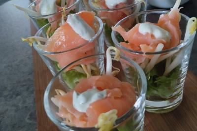 Plateau en bois avec verrines garnies, bol de pain tranché et bouteille de vin mousseux en arrière-plan.