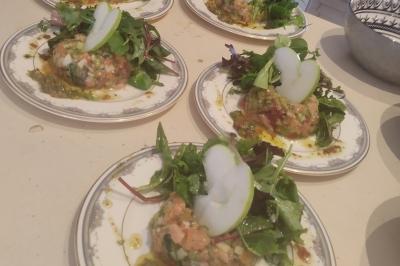 Plateau en bois avec verrines garnies, bol de pain tranché et bouteille de vin mousseux en arrière-plan.