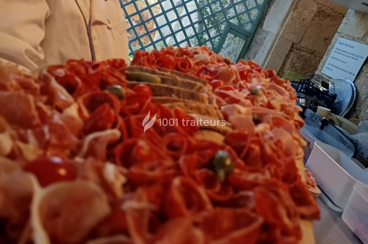 Plateau garni de charcuteries variées, tranches de pain et olives, présenté sur une table dans un cadre extérieur.