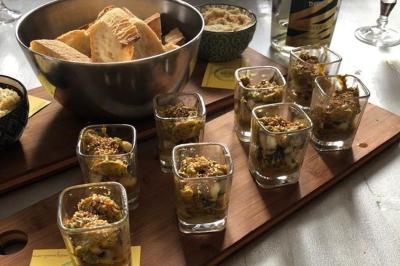 Plateau en bois avec verrines garnies, bol de pain tranché et bouteille de vin mousseux en arrière-plan.