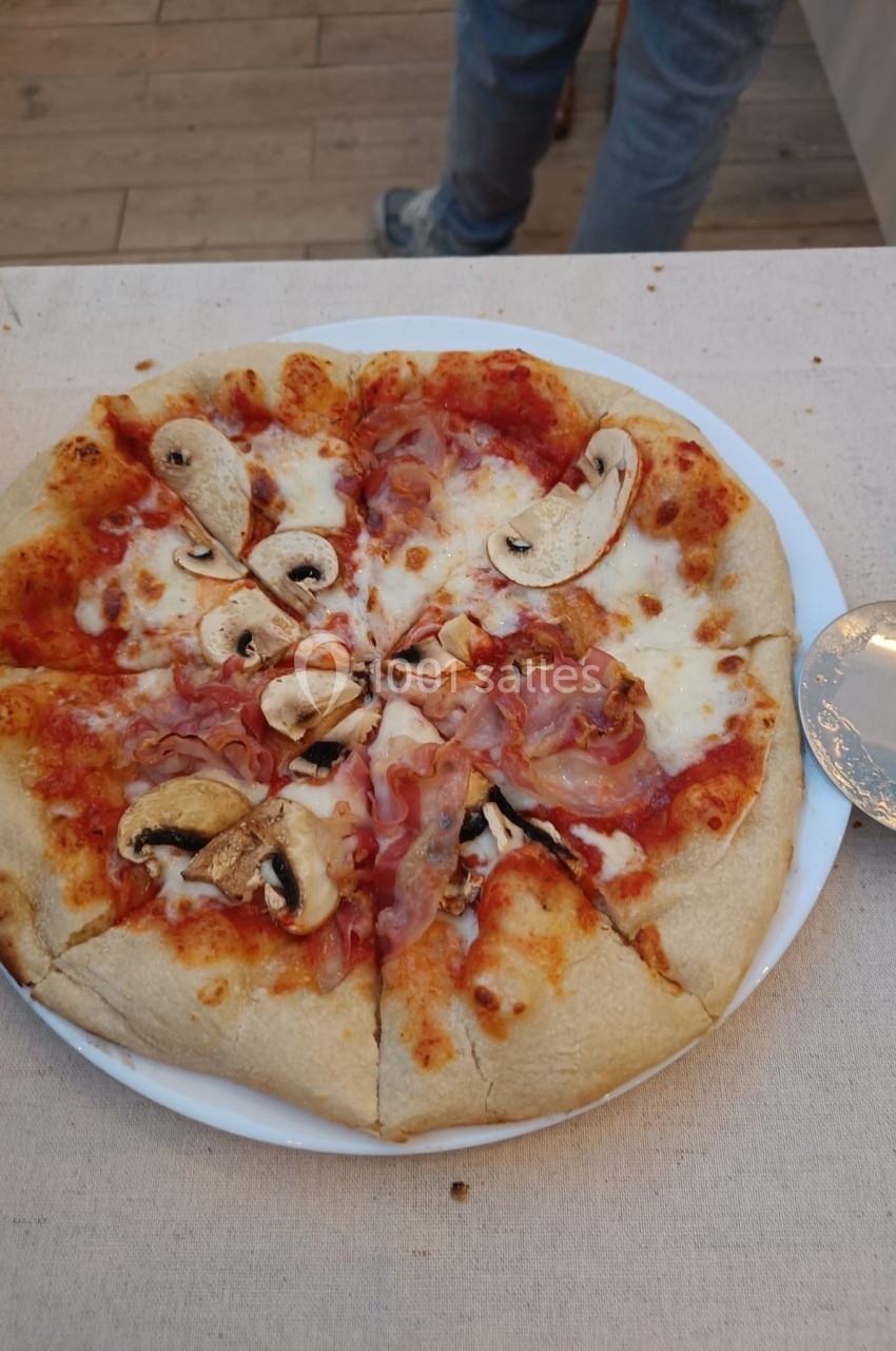 Pizza garnie de champignons, jambon et fromage, servie sur une assiette blanche avec une roulette à pizza à côté.
