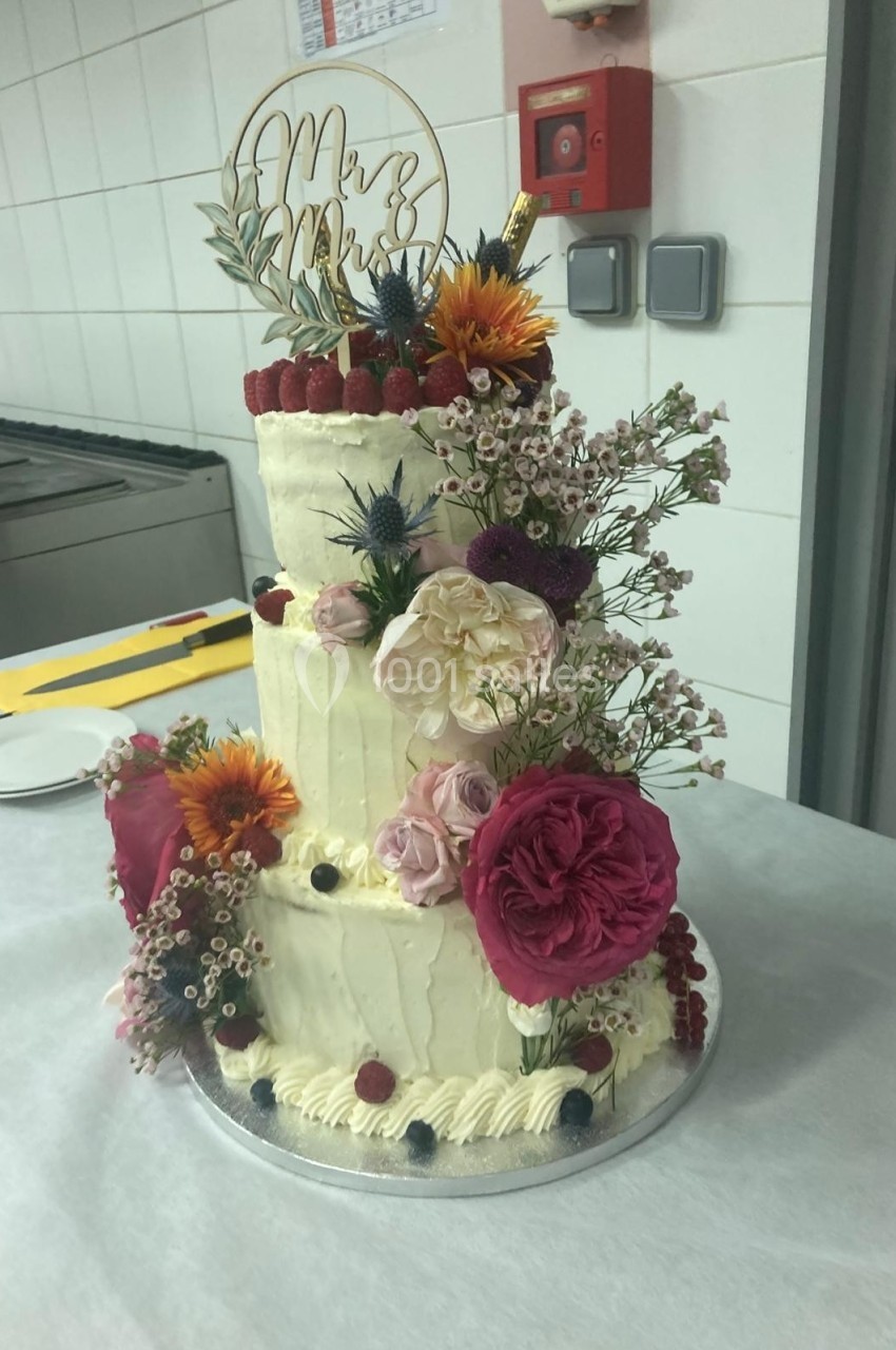 Gâteau de mariage à trois étages décoré de fleurs fraîches, de fruits rouges et d'un topper ’Mr & Mrs’.