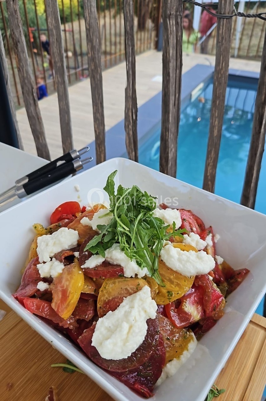 Salade de tomates colorées avec roquette et fromage frais, servie dans un bol près d'une piscine en extérieur.