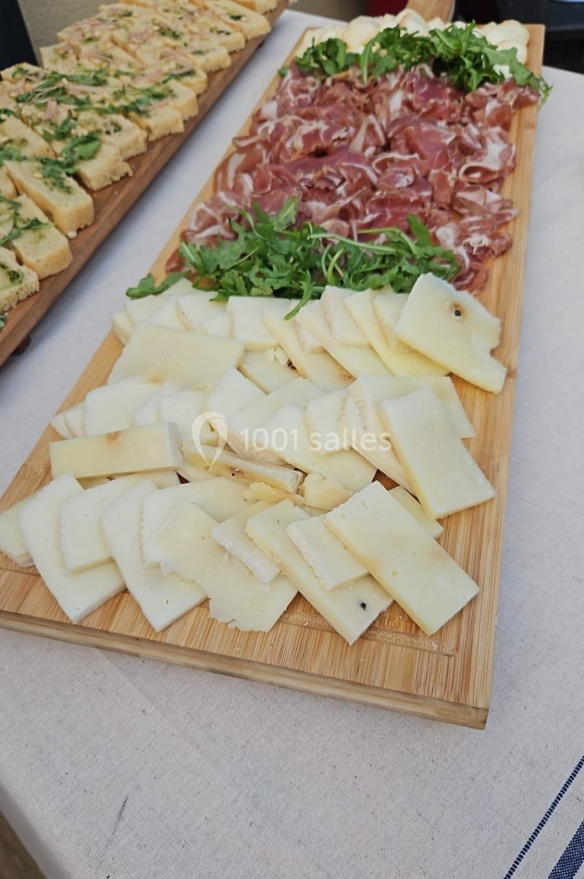 Plateau en bois avec tranches de fromage, charcuterie et roquette, accompagné de focaccia garnie en arrière-plan.