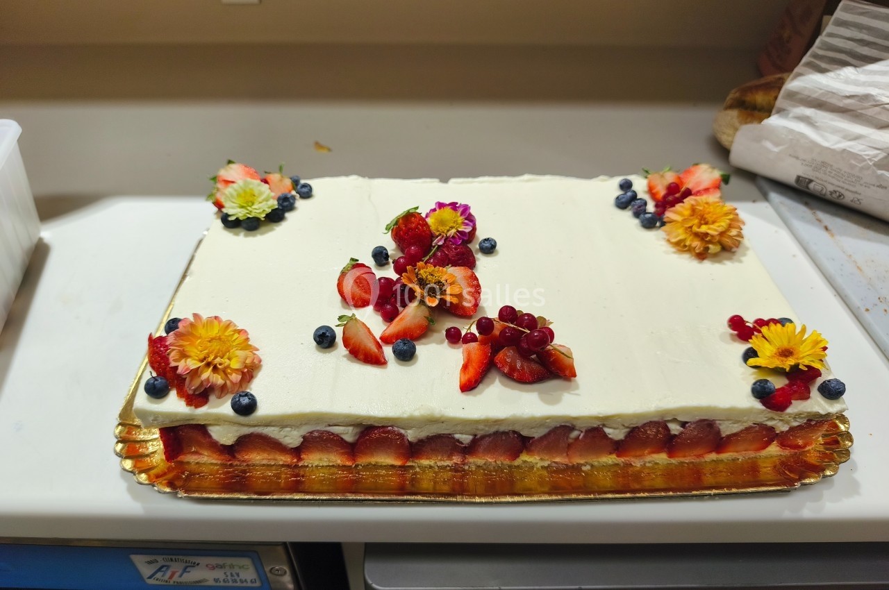 Gâteau rectangulaire décoré de fruits rouges, myrtilles et fleurs comestibles sur un glaçage blanc.