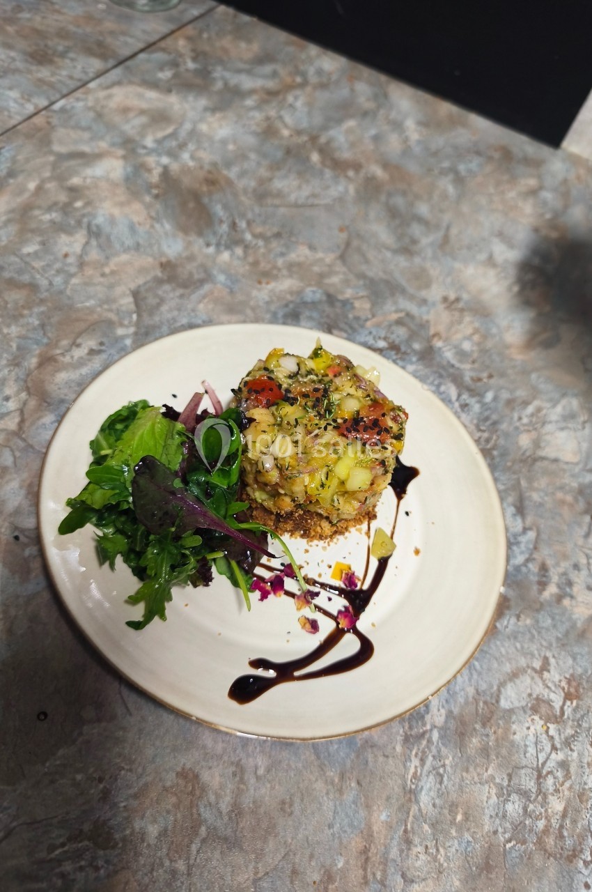 Assiette avec un tartare de légumes sur une base croustillante, accompagné de salade verte et d'un filet de sauce balsamique.